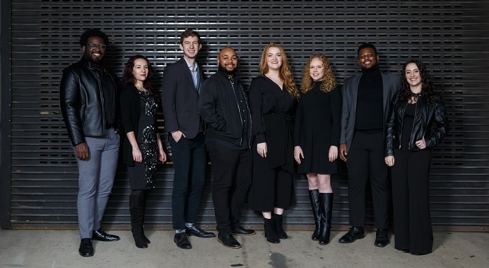 Pittsburgh Opera's 2021-22 Resident Artists all dressed in black or grey posing for a picture in front of a black wall