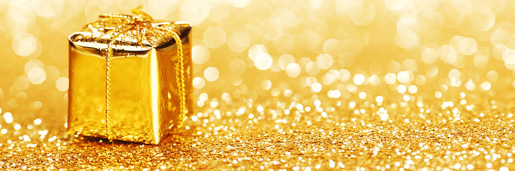 A gift in gold wrapping paper and bow sits on a golden glitter floor